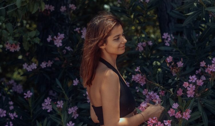 A woman in a black top smiles beside pink flowers in a garden.