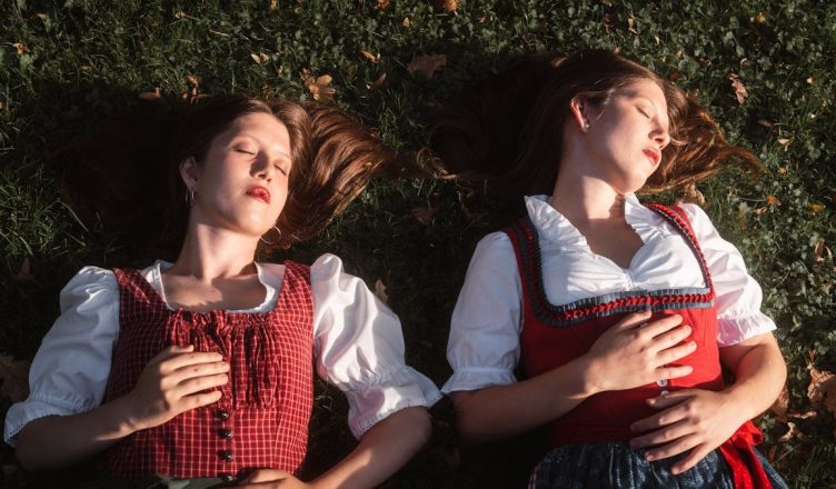 Two women in traditional European attire enjoying a peaceful moment in a grassy park in autumn.